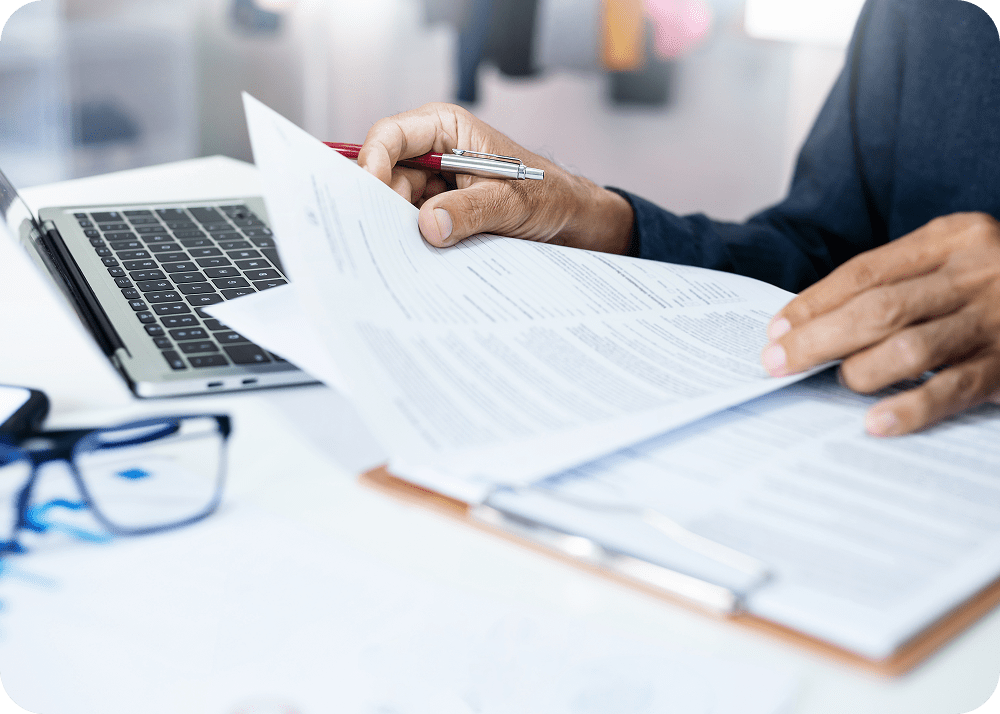 Hands reviewing documents near a laptop.